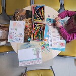 Dwie dziewczynki siedzą przy stoliku i wykonują pracę plastyczną na temat segregacji odpadów.