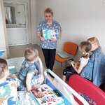Dzieci patrzą na kolorowo zilustrowany wiersz i słuchają jego treści czytanej przez nauczycielkę