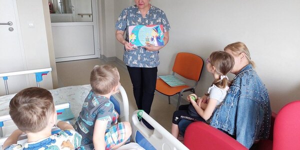 Dzieci patrzą na kolorowo zilustrowany wiersz i słuchają jego treści czytanej przez nauczycielkę