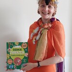 Nauczycielka w przebraniu za papugę prezentuje książkę z zadaniami o dzikich zwierzętach