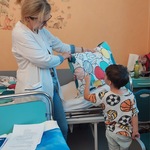 W Dniu Przedszkolaka chłopiec wskazuje na poduszce baloniki w podawanych przez nauczyciela kolorach