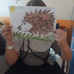 Chłopiec pokazuje portret jeża namalowany pastelami