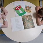 Dwoje dzieci siedzi przy stoliku, na którym leży książka z tekstem wiersza.