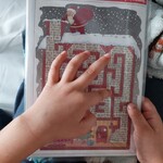 Dziecko wodzi palcem po labiryncie narysowanym na obrazku w tematyce mikołajkowo-świątecznej