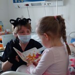 Nauczycielka w przebraniu za kotka, z pluszowym kotkiem i dziewczynka trzymająca książkę