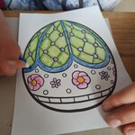 Uczennica koloruje niebiesko zieloną pisankę