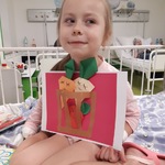 Dziewczynka siedząca w łóżeczku pokazuje swoją pracę: kosz z warzywami.