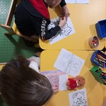 Chłopiec i dziewczynka siedzą przy żółtym stoliku i kolorują obrazki pluszowych misiów