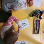 Dzieci siedzą przy żółtym stoliku i kolorują obrazki pluszowych misiów