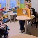 Nauczycielka siedzi przy stoliku w świetlicy kl. neurologii i przedstawia dzieciom teatrzyk kamishibai