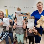Nauczycielki i dzieci w Dniu Misia trzymają kolorowanki przedstawiające misia