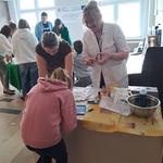 Dziewczynka  z mamą pochylone nad stołem i nauczycielka stojąca przy stole.