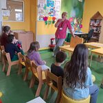 Nauczycielka prezentuje siedzącym przed nią dzieciom teatrzyk kamishibai i skrzynkę butai.