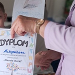 Nauczycielka wręcza dziecku dyplom za wykonanie pracy konkursowej Ł jak łabędź.