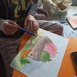 dziecko kredkami rysuje jeża z jabłkami zielonym i czerwonym na grzbiecie