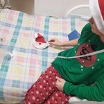 chłopiec siedzi na łóżku w mikołajkowej czapce trzymając w ręku wykonanego mikołaja z talerza