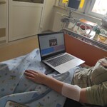 chłopiec siedzi na łóżku przed nim stoi włączony laptop