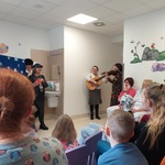 kobiety grają na skrzypcach i gitarze, przed nimi siedzą dzieci i rodzice