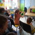 dzieci siedzą na krzesłach i oglądają teatrzyk