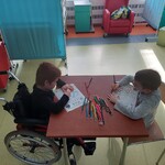 Przedszkolaki siedzą przy stoliku i kolorują kredkami pisankę