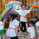 dziewczynka tańczy pośrodku koła trzymając w obu dłoniach kolorowe chusty