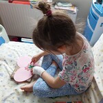 Dziewczynka lepi z plasteliny kwiatki na papierowym różowym serduszku
