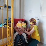 Dziecko z mamą słucha opowieści o kaczuszce czytanej przez nauczycielkę w kaczym przebraniu