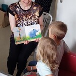 Przedszkolaki oglądają ilustracje w książce o dzikich zwierzętach i słuchają nauczycielki, która o nich czyta