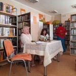 sala biblioteczna przy regale z książkami stolik przy nim siedzą dwie kobiety