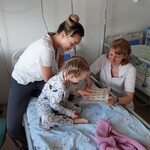 Dziecko w obecności mamy i nauczycielki wykonuje zadanie obrazkowe w Dniu Przedszkolaka