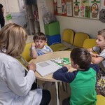 Nauczycielka prezentująca wiersz i trzech chłopców siedzą przy stoliku w świetlicy.