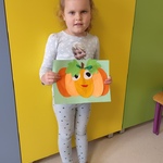 Dziewczynka stojąca na tle żółtych szafek prezentuje swoją pracę- dynię.