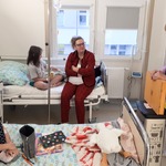 W sali szpitalnej dwie dziewczynki i mama siedzą na łóżkach, a nauczycielka prezentuje skrzynkę teatrzyku kamishibai.