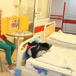 Nauczycielka siedzi w sali szpitalnej i czyta bajkę w teatrzyku kamishibai.