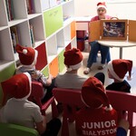 Nauczycielka przedstawia bajkę dzieciom zgromadzonym w świetlicy oddziałowej. Wszyscy mają założone czapki mikołajkowe.