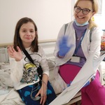 dziewczynka i nauczycielka siedzą na łóżku i machają na powitanie rękami