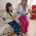 dziewczynka siedząc na łóżku ogląda książkę o radości obok siedzi nauczycielka