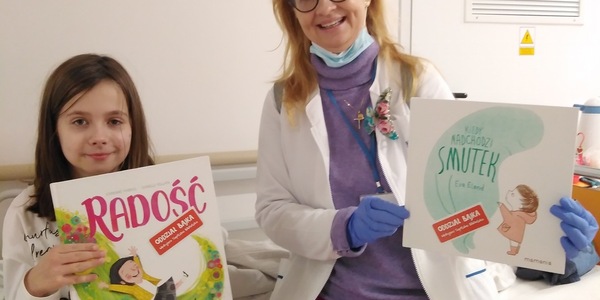 dziewczynka trzyma przed sobą książkę radość obok niej nauczycielka trzyma przed sobą książkę gdy nadchodzi smutek