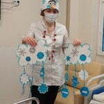 Nauczycielka w przebraniu za bajkowego Olafa, ubrana w czapkę z dzwoneczkami na szyi, trzyma chmurki z zawieszonymi śnieżynkami, które kryją zimowe zagadki